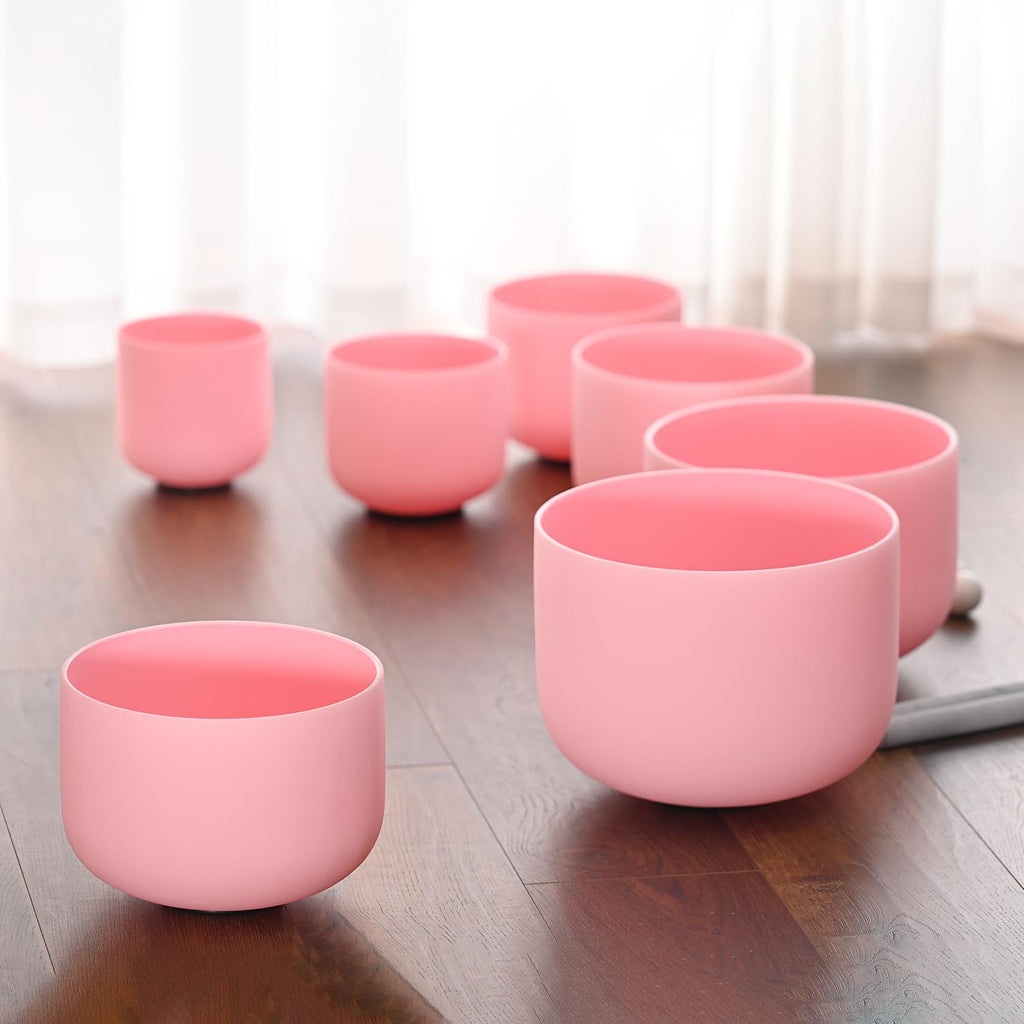 Pink frosted crystal singing bowls, multiple sizes, arranged on a wooden floor