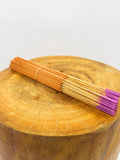 Incense sticks with light orange stems and purple tips on a wooden slab