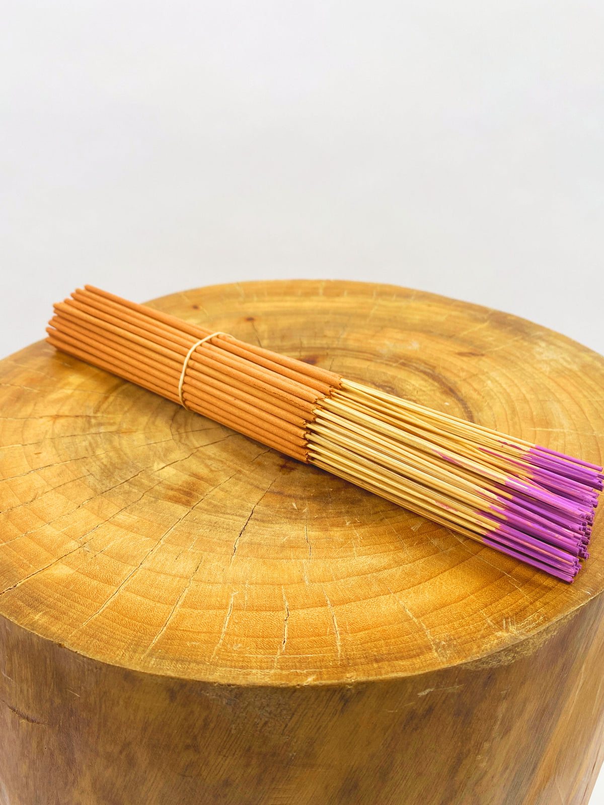 Incense sticks with light orange stems and purple tips on a wooden slab