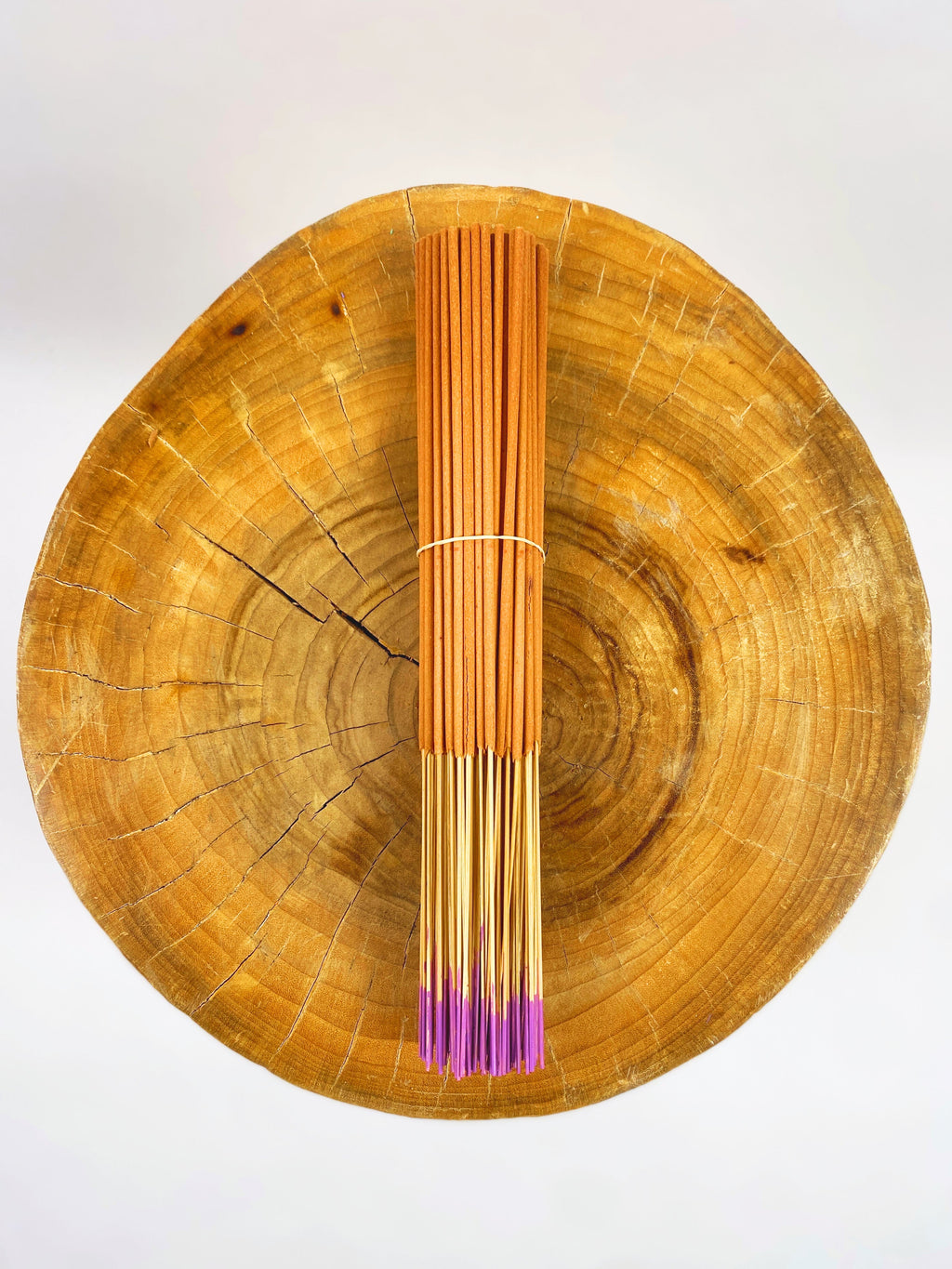 Incense stick bundle with purple ends held upright on a round wood slice
